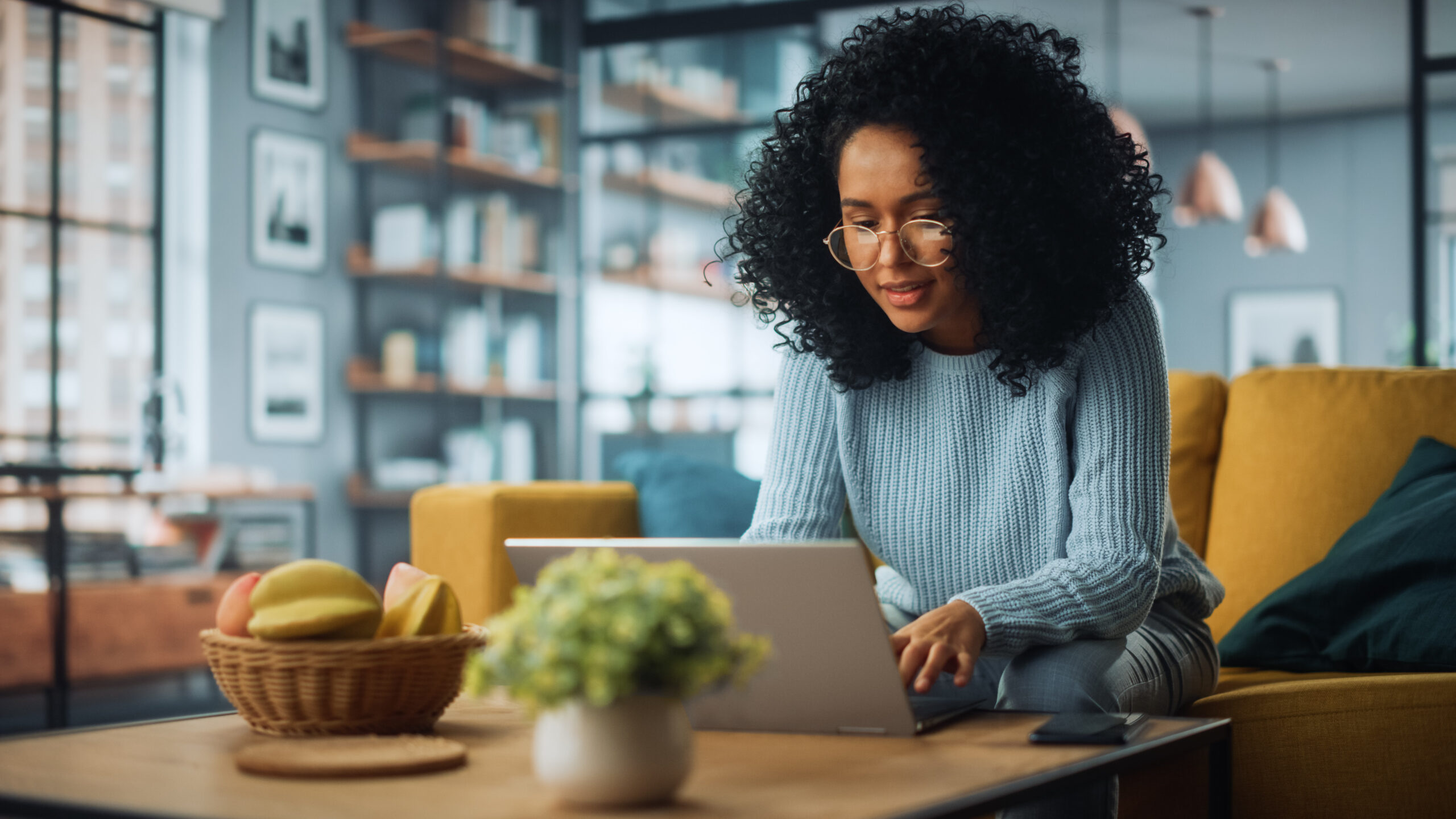 Beautiful Authentic Latina Female Sitting on a Sofa in a Cozy Living Room and Using Laptop Computer at Home. Happy Freelancer Female Browsing Internet and Social Networks.